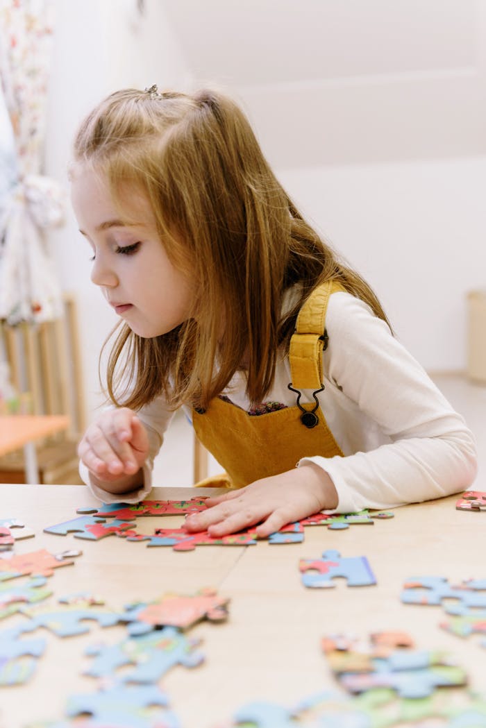 Young girl focused on assembling colorful puzzle pieces indoors, wearing yellow overalls.